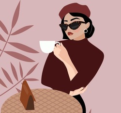 A Young Beautiful Brunette Woman With A Short Hairstyle In A Beret Sits In A Cafe And Drinks Coffee. French Style In Clothes. Fashionable Girl With Sunglasses Holds A Cup Of Hot Drink, Tea, Coffee