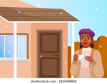 Young black smiling woman in winter clothes standing on the cottage background and drinking hot coffee. Winter time, snow-flakes. Young house girl with modern makeup on the private house background