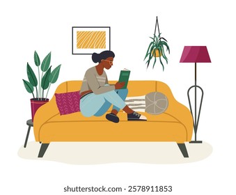 Young black woman is reading a book sitting on a comfortable yellow sofa in her living room, enjoying her free time surrounded by houseplants and a modern floor lamp