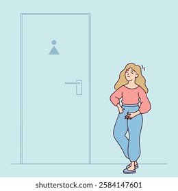 Young blonde woman with long hair stands near a toilet door, appearing uncomfortable. She is urgently waiting