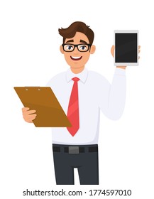 Young business man in eye glasses holding clipboard and showing tablet computer screen. Trendy person carrying document, file, checklist. Male character keeping folder. Cartoon illustration in vector.