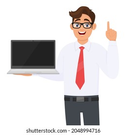 Young Business Man Showing A Laptop And Pointing Hand Finger Up. Person Carrying Computer (PC). Male Character Holding Digital Technology Device. Modern Lifestyle Illustration In Vector Cartoon.