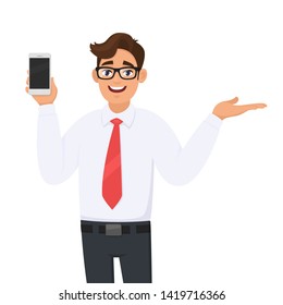 Young business man showing new brand, latest smartphone. Man holding cell, mobile phone in hand and gesturing/presenting hand palm to copy space side away. Modern lifestyle, digital technology device.