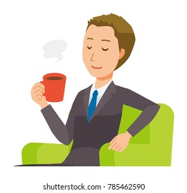 A young businessman is sitting on the sofa and drinking coffee