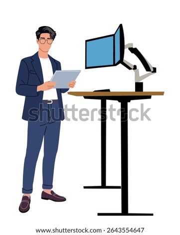 Young businessman in suit and glasses stands with digital tablet near ergonomic standing desk with dual monitors. Modern office, tech-savvy workspace, productivity concept