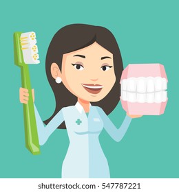 Young Caucasian Female Dentist Holding Dental Jaw Model And A Toothbrush In Hands. Friendly Female Dentist Showing Dental Jaw Model And Toothbrush. Vector Flat Design Illustration. Square Layout.