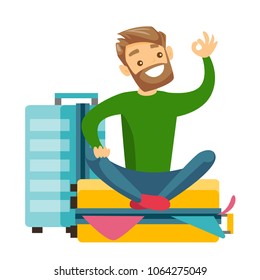 Young Caucasian White Man Sitting On A Suitcase Full Of Clothes And Trying To Close It. Happy Man Packing A Lot Of Clothes Into A Single Suitcase And Showing Ok Sign. Vector Cartoon Illustration.