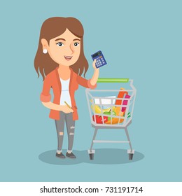 Young caucasian woman standing next to the supermarket trolley full of products and holding a calculator in hand. Woman checking prices on a calculator. Vector cartoon illustration. Square layout.