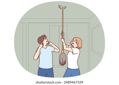 Young couple bangs on ceiling with mop urging neighbors to stop party or turn off loud music. Angry men and women use mop suffer from noisy neighbors not respecting rules of living together