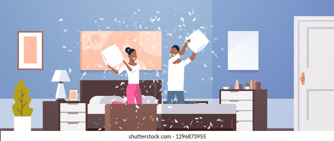 young couple having pillow battle african american man woman enjoying time together lovers beat with pillows on bed at home modern apartment bedroom interior horizontal flat