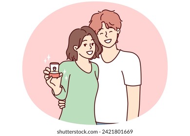 Jóvenes pareja de hombres y mujeres se paran en abrazo y miran la cámara mostrando la caja con el anillo de boda. Novia y novio con ropa informal luego de una propuesta para la vida familiar conjunta. Ilustración vectorial plana