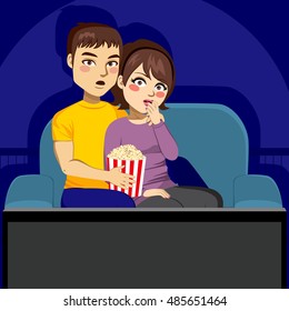 Young Couple Sitting On Couch Watching Scary TV Movie At Night In Dark Living Room