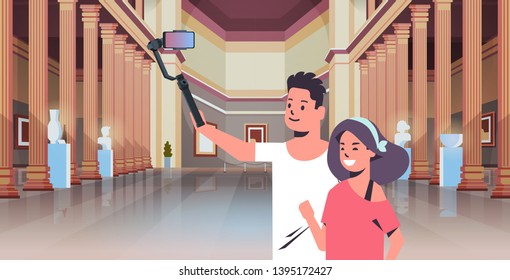 young couple using selfie stick taking photo on smartphone camera man woman visitors in modern art gallery museum hall interior portrait horizontal