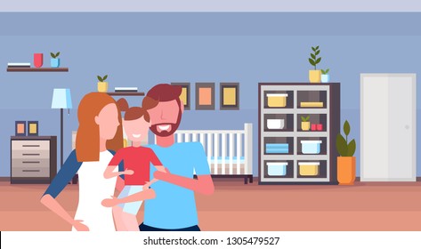 young family loving parents holding little son at home baby bed newborn room wooden crib kid bedroom interior cartoon characters portrait horizontal flat