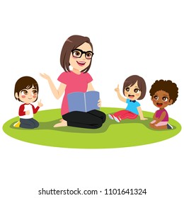 Young female kindergarten teacher explaining lesson reading book to attentive kids sitting on floor