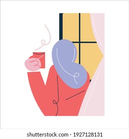 Young female standing with cup of hot drink and looking at window at home in morning