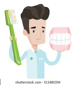 Young friendly dentist holding dental jaw model and a toothbrush in hands. Caucasian male dentist showing dental jaw model and toothbrush. Vector flat design illustration isolated on white background.