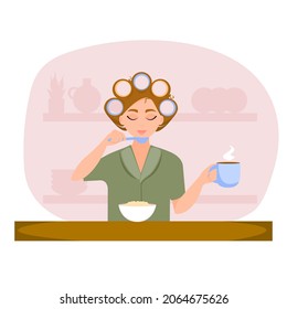 Young girl with curlers is having breakfast in the kitchen. Concept of morning routine.
