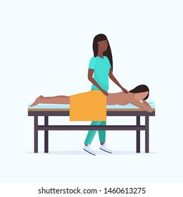 young girl having back massage african american masseuse therapist in uniform massaging patient body woman relaxing lying on bed spa salon treatments concept full length