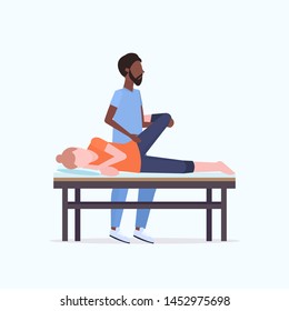 Young Girl Lying On Massage Bed African American Masseur Therapist Doing Healing Treatment Massaging Patient Treating Legs Manual Sport Physical Therapy Concept Full Length