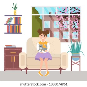 A young girl is resting with a gray cat sitting on her lap. A pet owner is stroking a small kitty. The child sits at home near the window against the background of sakura, playing with domestic animal