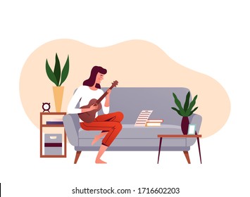 Young girl sits on a couch and learns to play the ukulele on notes. Concept of learning music at home. Home daily activities