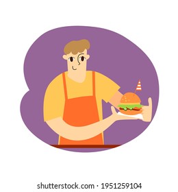 Un joven de un delantal naranja sostiene una hamburguesa con una bandera a rayas en las manos. Vendedor de comida rápida. Ilustración plana del vector