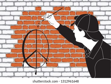 A young guy painter in the cap draws signs on the brick wall