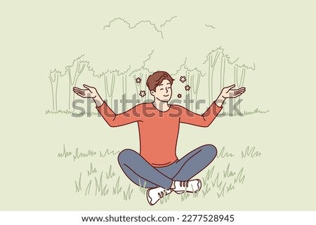 Young guy sits in lotus position on lawn doing yoga and meditating to restore strength or improve mood. Man practices yoga enjoying harmony and following recommendations Buddhist spiritual teachings