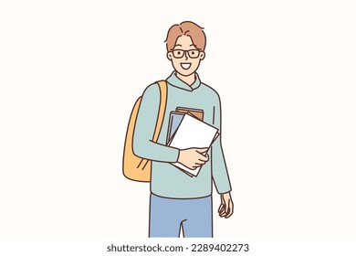 Young guy student with books and backpack is preparing for hike from campus to college or university. Student or schoolboy student in high school ready for exams smiling and looking at camera 