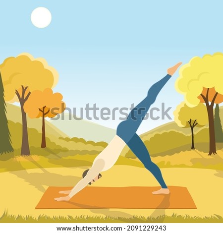 Young handsome man is doing yoga, standing in Eka Adho Mukha Svanasana or one-legged downward facing dog pose on the mat in the autumn park with mountines.
