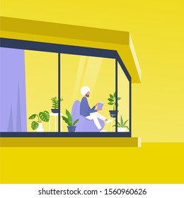 Young indian male character reading a book in front of the window inside a modern house, outside view