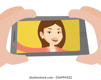 Young joyful caucasian woman making selfie. Smiling woman making selfie with cellphone. Woman taking selfie. Vector flat design illustration isolated on white background.