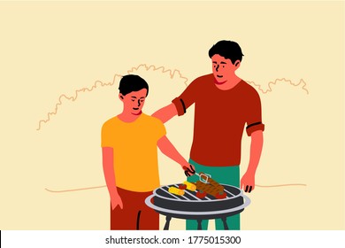  Young man dad teaching child kid son how to grill standing together in backyard. Family gathering and spending time on summer vacation or fathers day