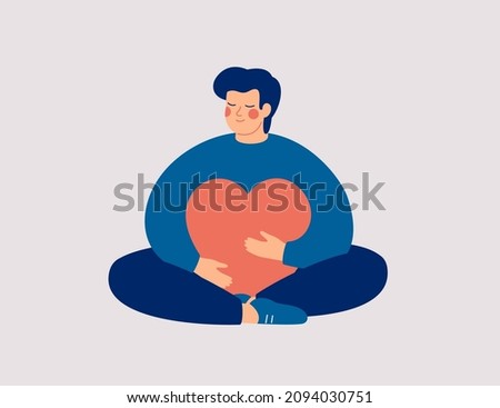 Young man embraces a big red heart with mindfulness and love. Smiling boy sits in lotus pose with closed eyes and enjoys his freedom and life. Body positive and mental health concept. 