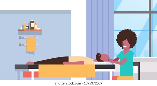 young man having head massage african american masseuse massaging patient body guy relaxing lying on table luxury spa salon medical clinic cabinet interior treatments concept horizontal