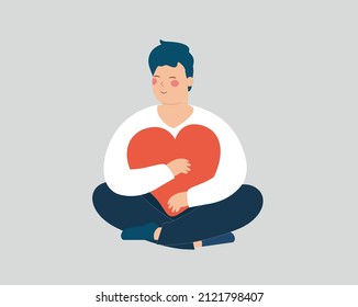 Young man holds, hugs a big heart. Happy adolescent boy sits in lotus pose with closed eyes. Male and cares a red heart with love while sitting. Self acceptance, positive body mental health concept.