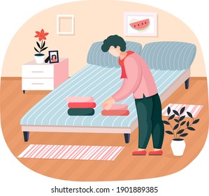 Young man householder puts bedclothes in order at home standing near bed in bedroom neatly stacks laundry. Household affairs tidy home. Family members activity for order things in their places