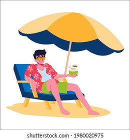 A young man lounged comfortably on a beach chair under large umbrella to block the sunlight on a summer vacation.