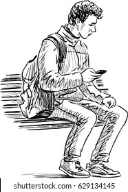 young man with a mobile phone sits on a park bench