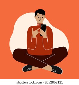 Young man on the phone sitting cross-legged and points finger at the phone screen