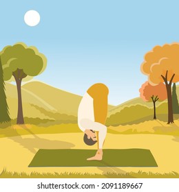 Young man performing Uttanasana pose or standing forward bend, working out outdoors on the autumn day in the beautiful park. 