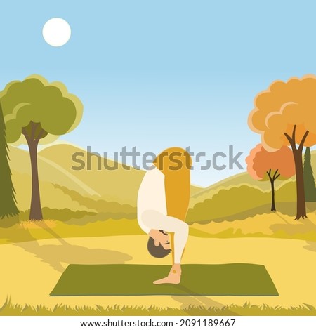 Young man performing Uttanasana pose or standing forward bend, working out outdoors on the autumn day in the beautiful park. 