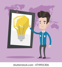 Young man pointing at a big tablet computer with a light bulb on a screen. Smiling man standing near tablet computer on a background with world map. Vector flat design illustration. Square layout.