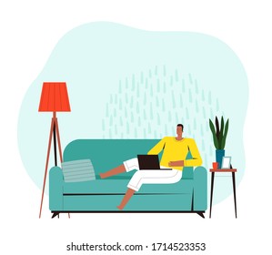 Young man sits on a sofa and works or plays on a laptop. The concept of home office and comfortable remote work. Home daily activities
