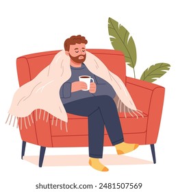 Young man sits on the sofa with a cup of tea wrapped in a blanket and is sick.