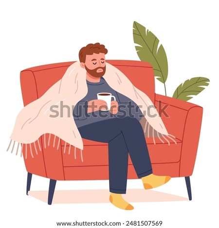 Young man sits on the sofa with a cup of tea wrapped in a blanket and is sick.