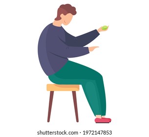 Young man sitting on chair and holding green coins on white background. Guy points his finger and plays game. Person in blue pants and purple sweater. Boy resting and playing table game alone