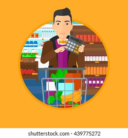Young man at the supermarket with calculator and supermarket trolley full with products. Man checking prices with calculator. Vector flat design illustration in the circle isolated on background.