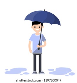 A young man with an umbrella in the rain. Drops of water fall down. Autumn weather and slush. Puddles on the ground.

